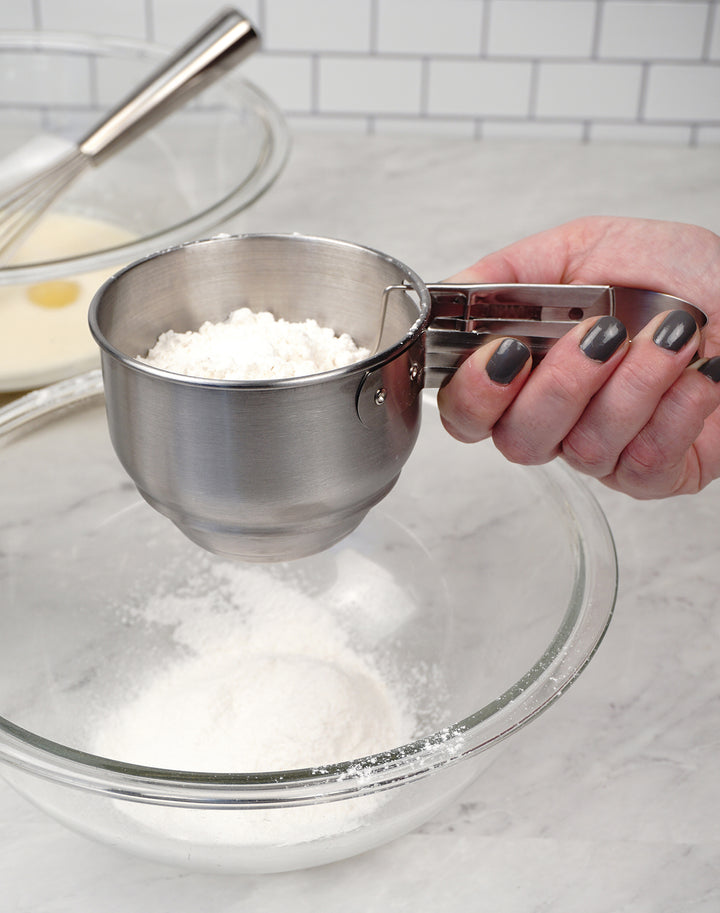 hand holding Vintage Style Sifter filled with flour over a bowl.