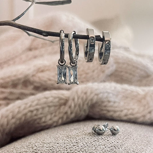 silver Waterproof Charm Hoop Earring Trio arranged on a twig with a sweater in the background