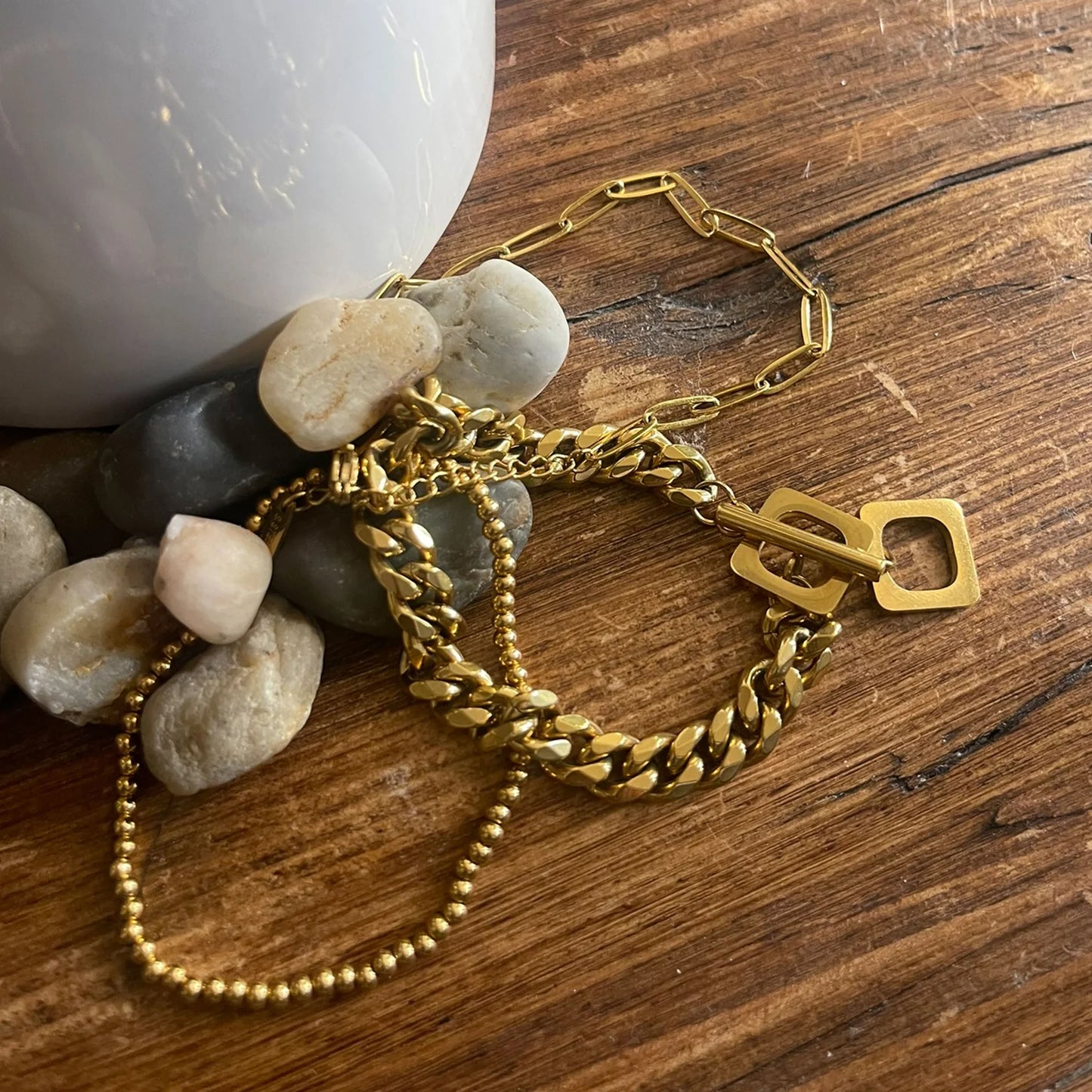 gold Waterproof Curb Chain Bracelet Set laying on a table with pebbles