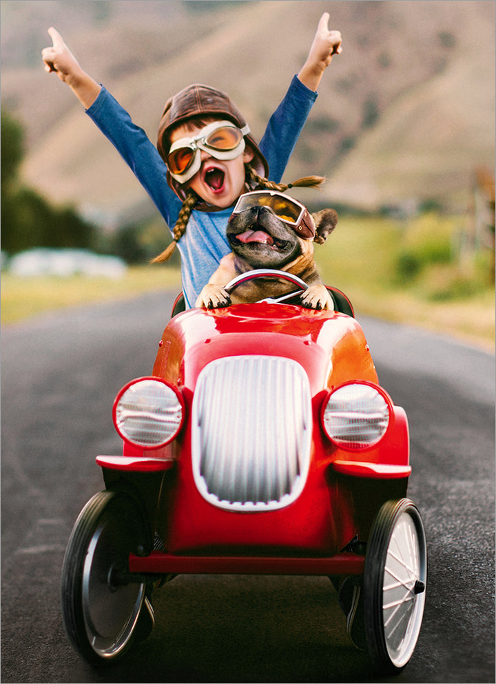front of card has a little kid with their hands in the air and a dog riding in a small red go cart car