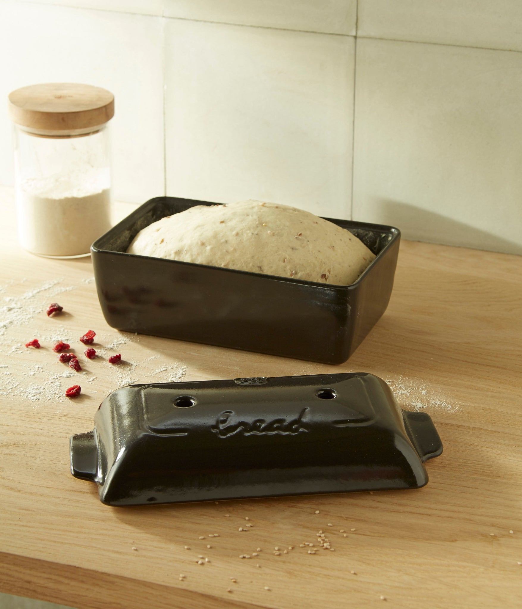 loaf baker with bread dough in it set on a counter with the lid and a canister of flour.
