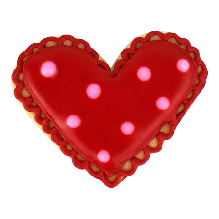 Heart-shaped cookie with red icing and pink polka dots on a white background