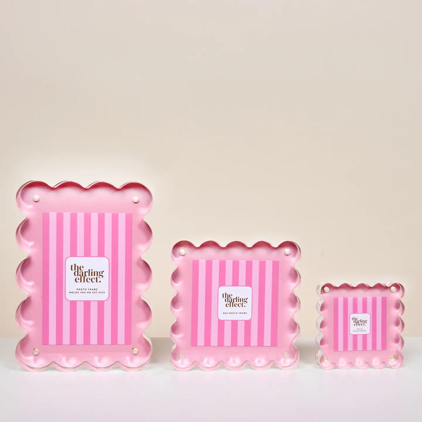 Three pink scalloped-edge frames in different sizes, arranged on a white surface against a light beige background.