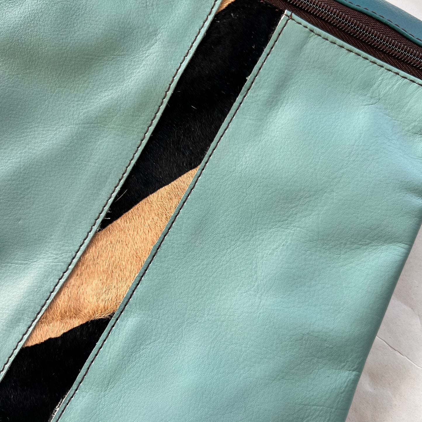 close-up of blue greta bag with animal print stripe down the center and zipper at the top.