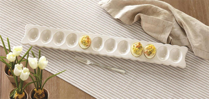 scalloped deviled egg tray with 3 eggs in it set on a table with a grey striped runner, pots of tulips, and a serving fork next to it.