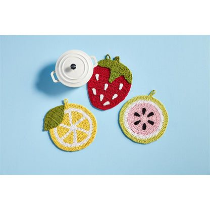 3 fruit shaped crochet trivet arranged on a blue background with a mini baker.