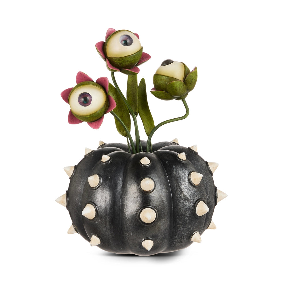 Black pumpkin with white spikes on it and three floral stems coming out of it with eyeballs in their center