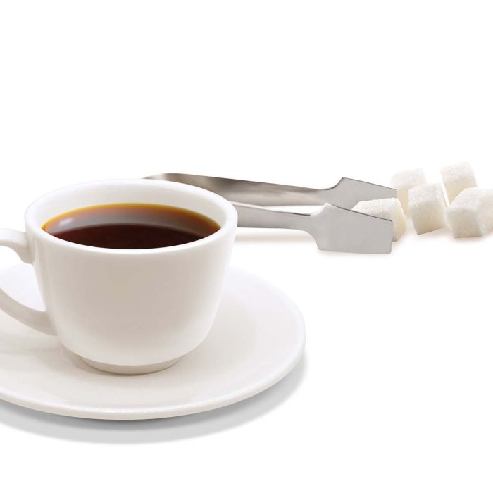 cup of coffee with sugar cubes and tongs set near it