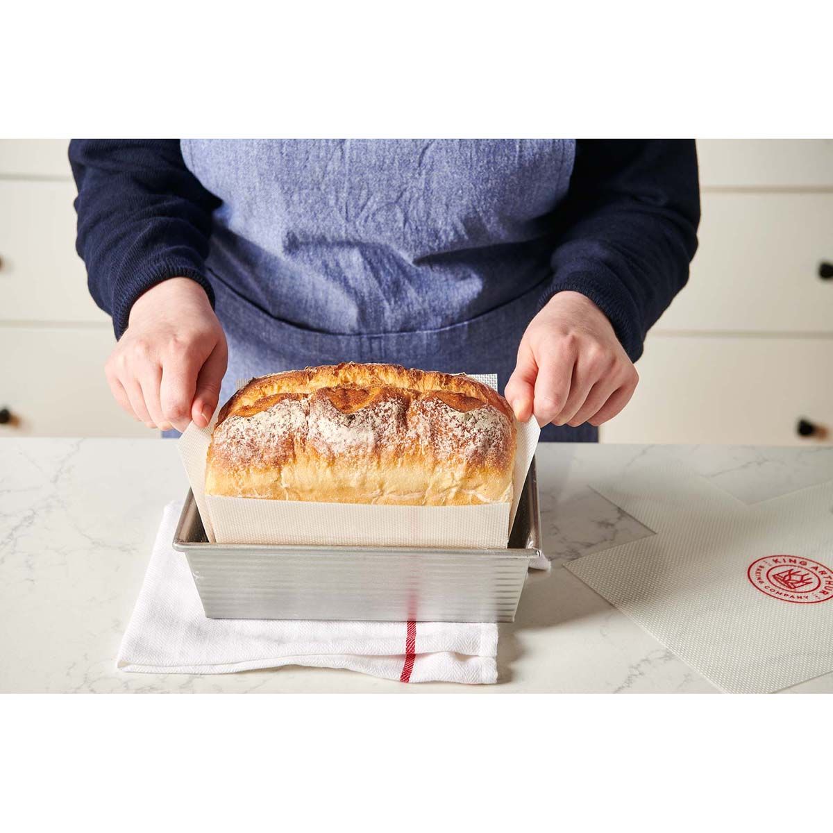 person removing baked loaf from pan with liner