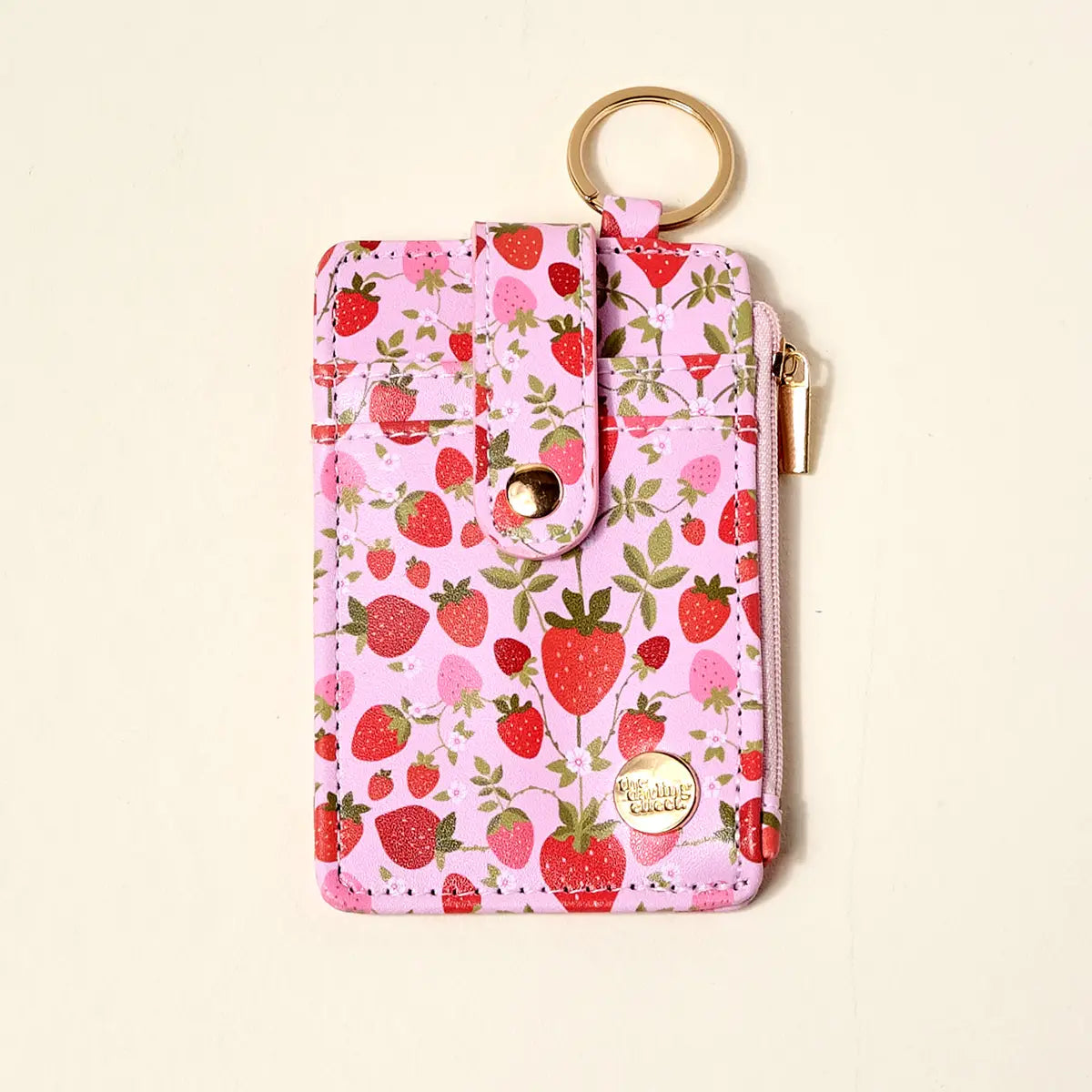 Pink wallet with strawberry pattern and gold key ring on a beige background