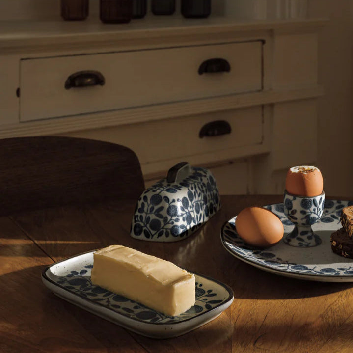 tray of butter with dome set behind it on a wooden table with other dishes
