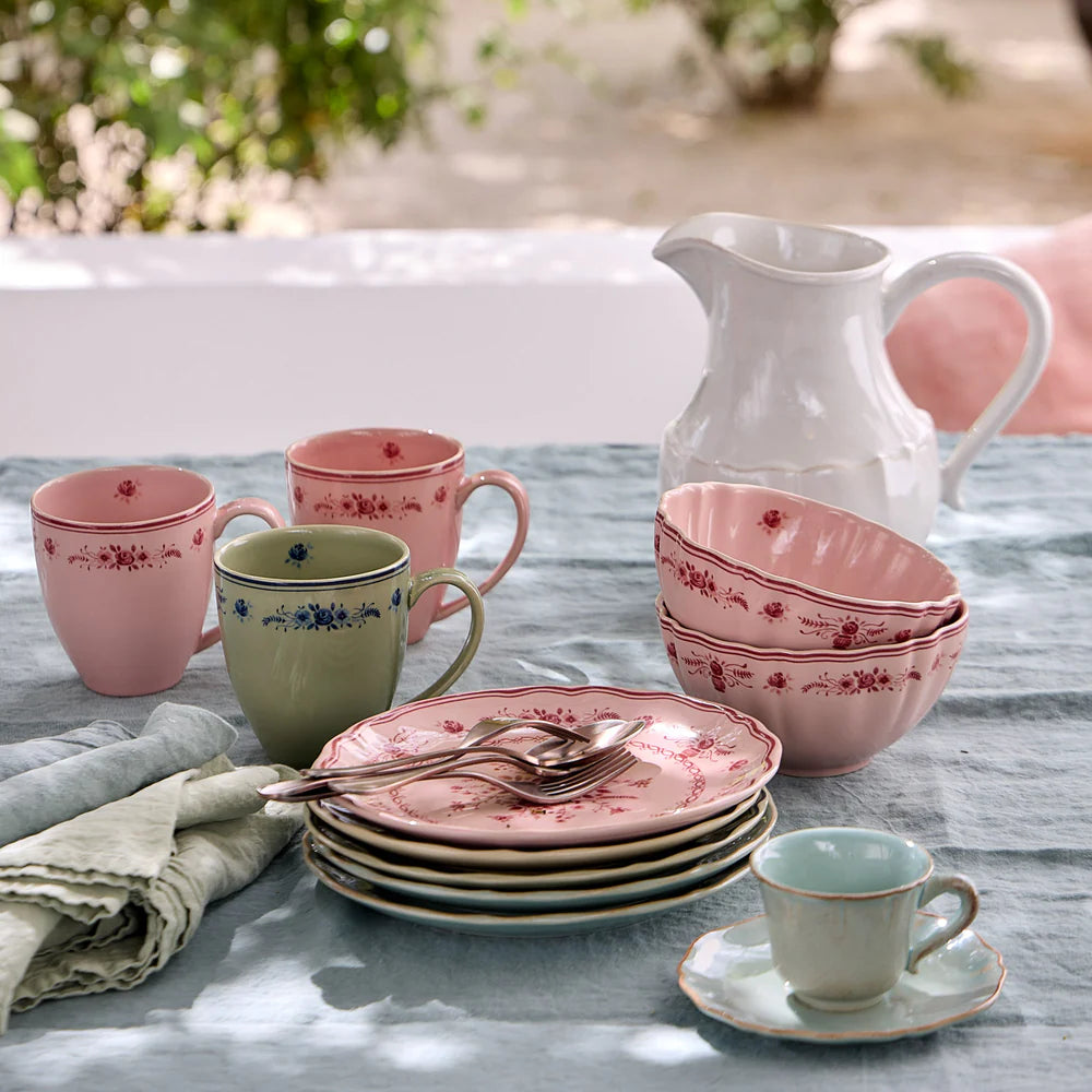 Ceramic tableware set with pink and red floral patterns on a wooden table.