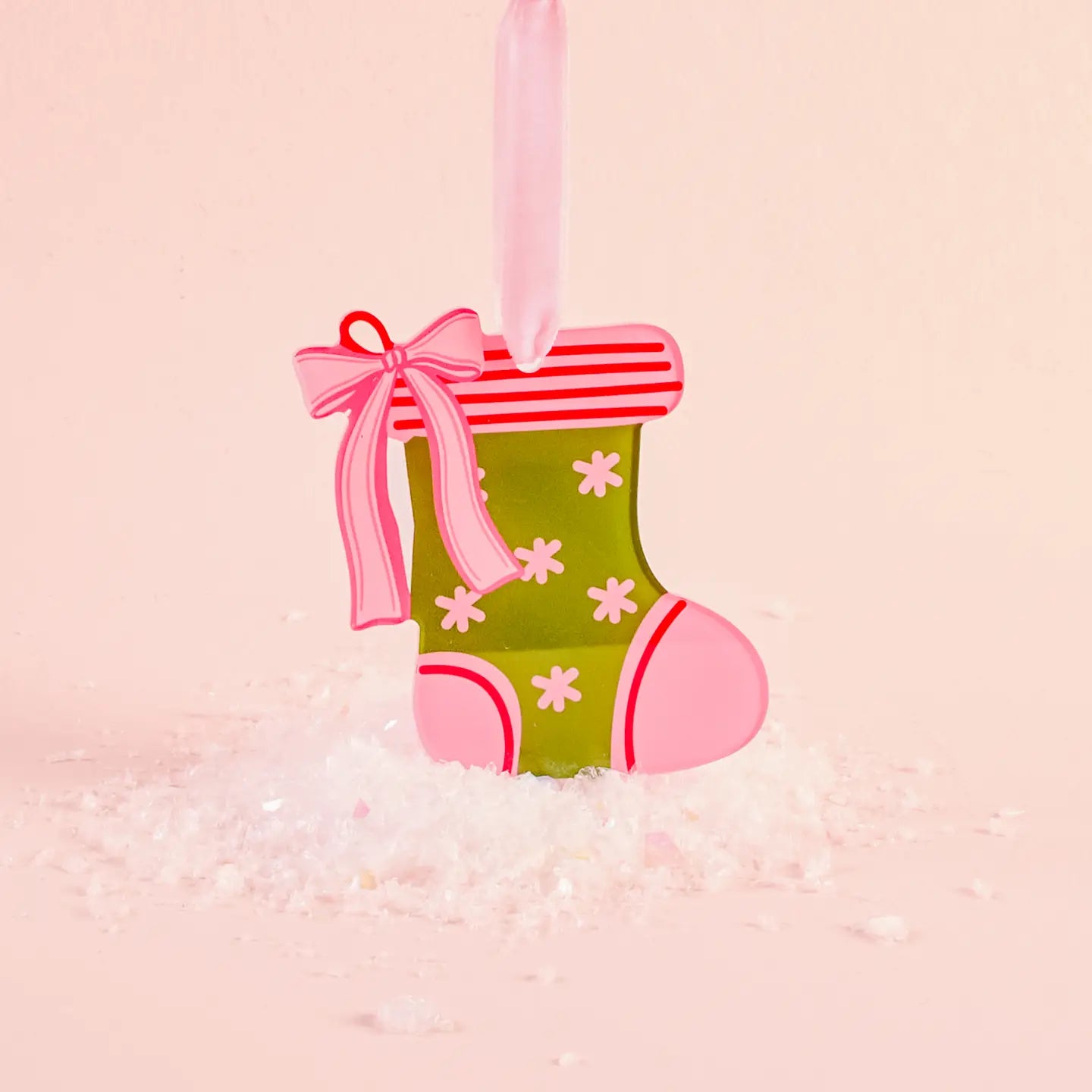 green acyclic stocking ornament with pink trim and a bow set with artificial snow on a pink background