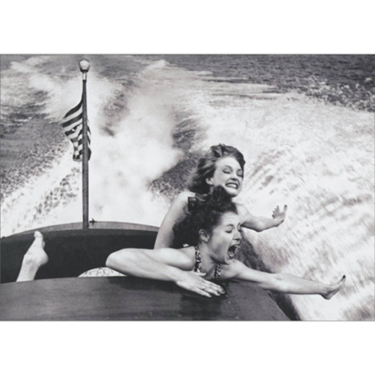front of card is two women holding their arms out while riding in a boat with an american flag on the back
