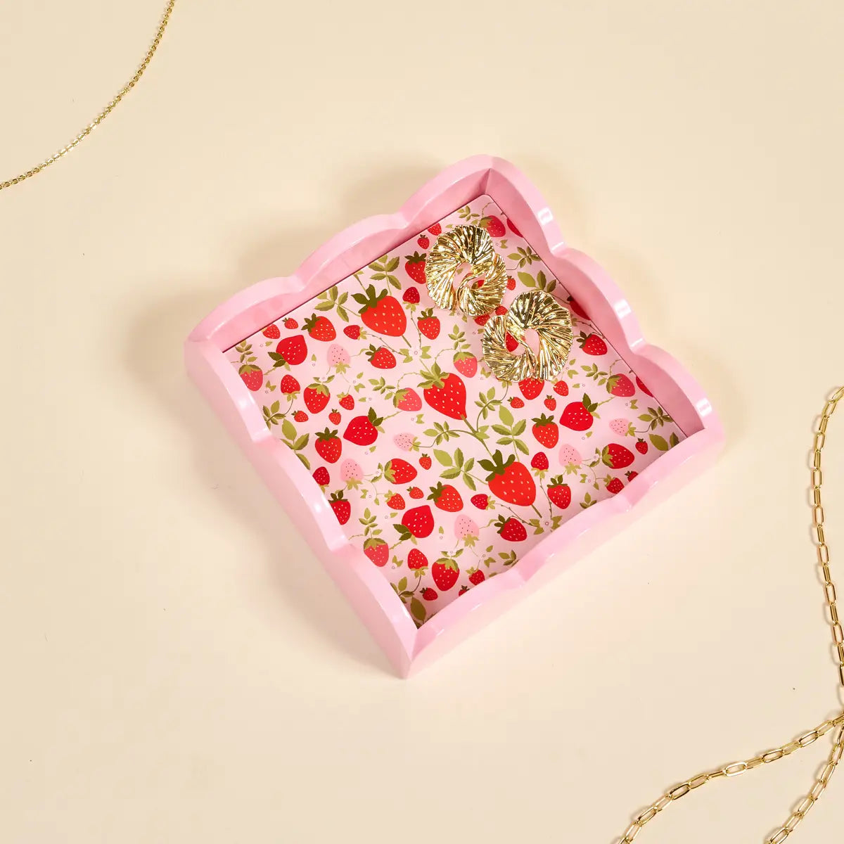 small tray with strawberry pattern with gold earrings in it shown on a beige background