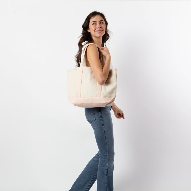 a person wearing jeans and white top holding off white tote with pale pink trim and handles