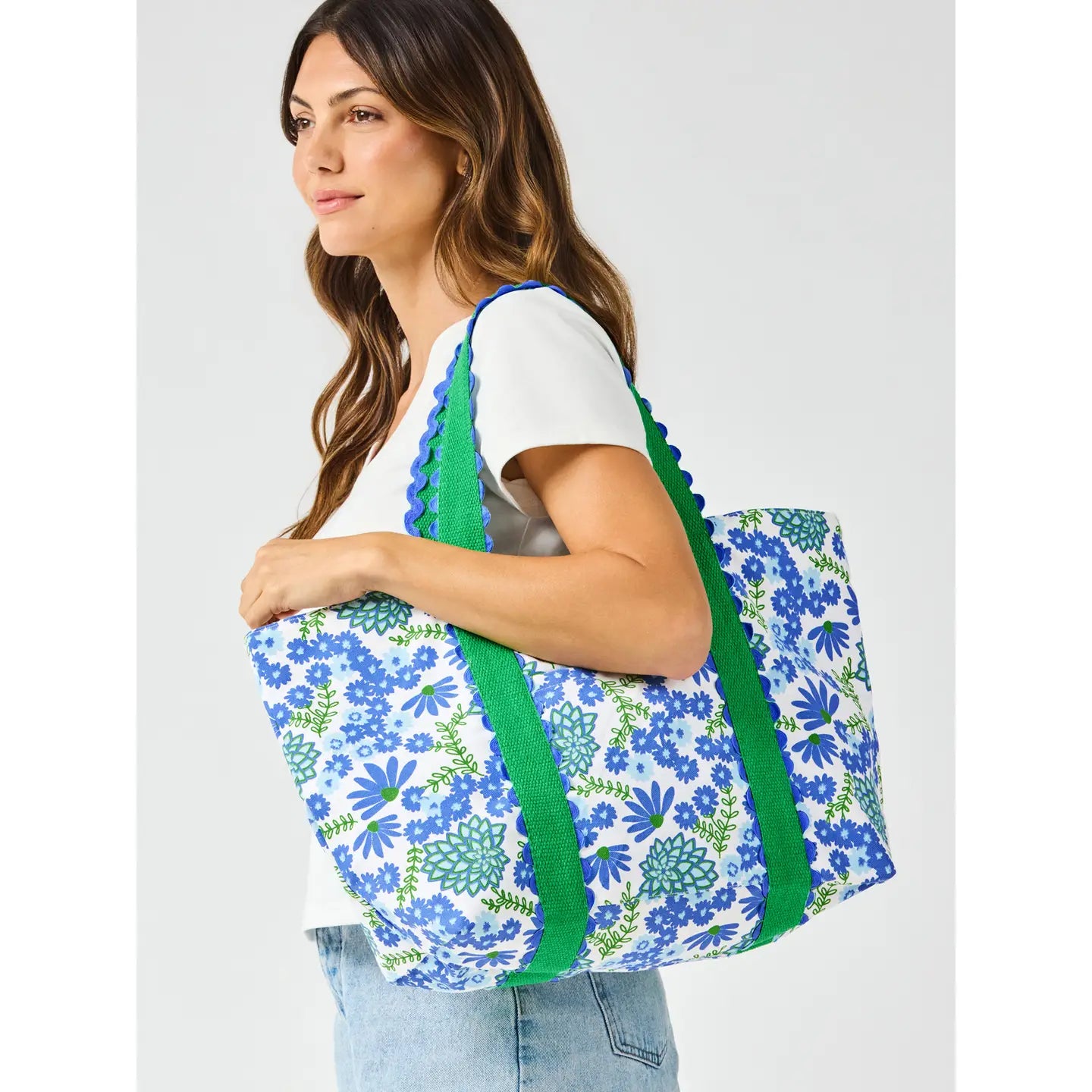 person holding a floral-patterned bag with green straps on a white background