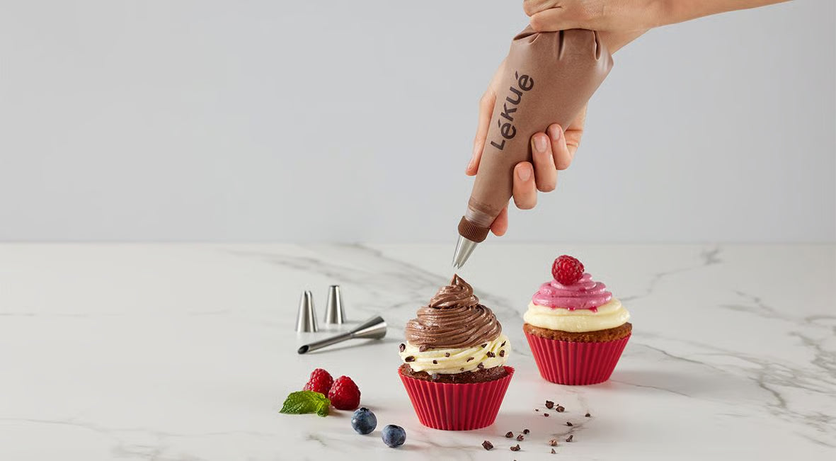hands holding icing bag and putting chocolate icing on cupcakes set on a marble counter