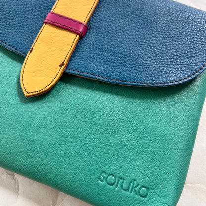 close-up of seafoam saddle bag with blue flap and yellow tab.
