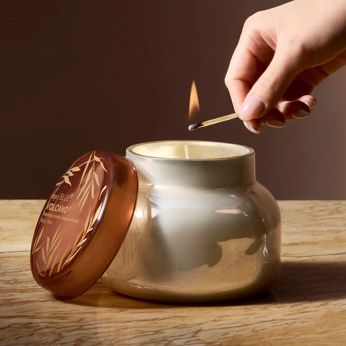 a hand lighting the autumn glow volcano candle