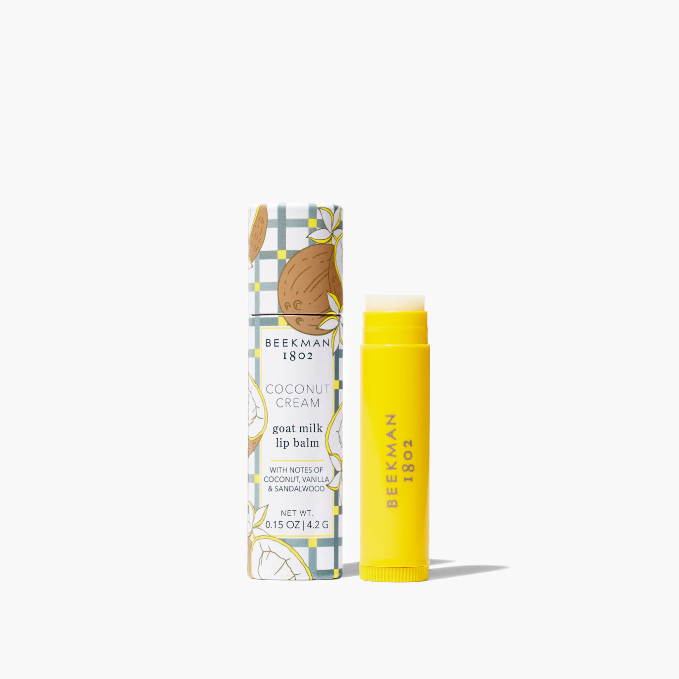 yellow tube of lip balm set next to its tube packaging printed with coconut and grey check design