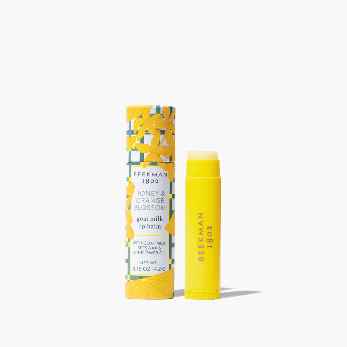 yellow tube of Honey & Orange Blossom Lip Balm set next to its tube packaging with and orange blossom and grey check design