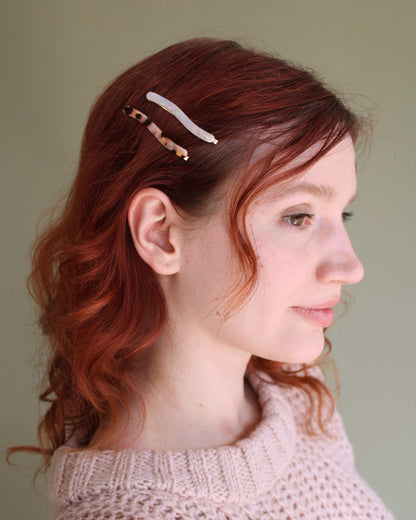 person with red hair wearing 2 bobby pins on one side holding their bangs back.