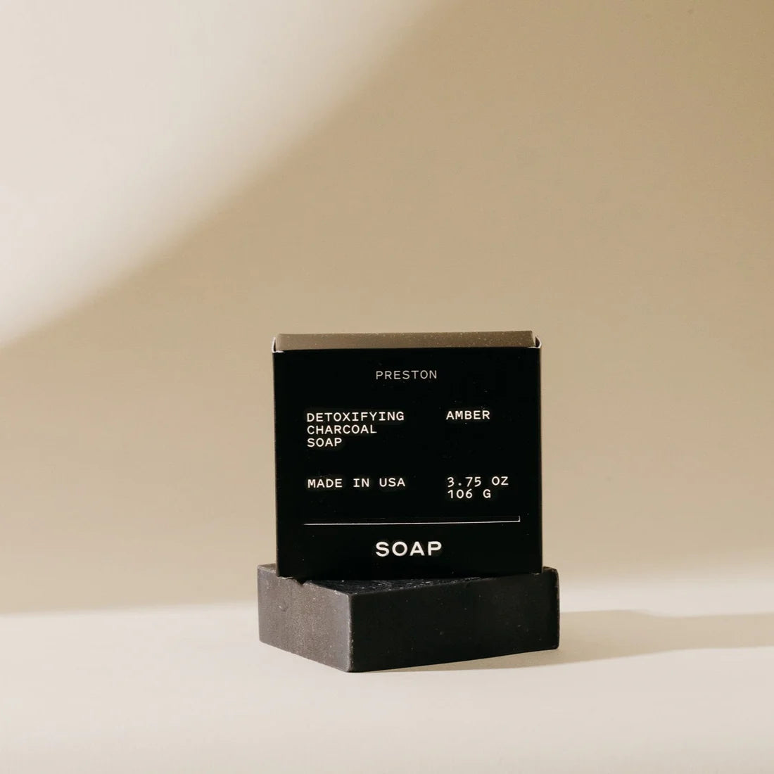 black bar of soap with packaging set on top of it on a beige background