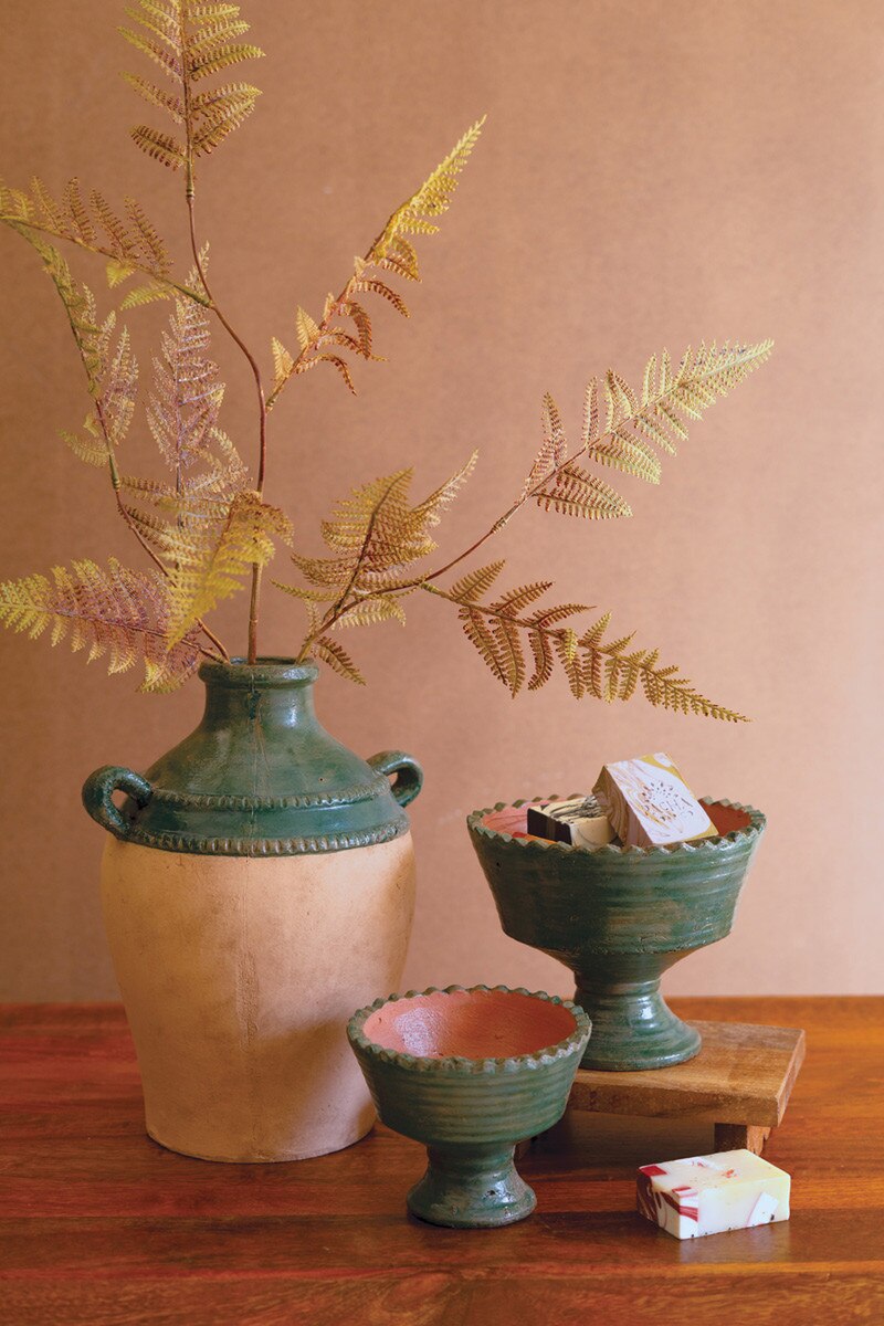 Decorative setting with ceramic vases, compotes, and a fern on a wooden surface.