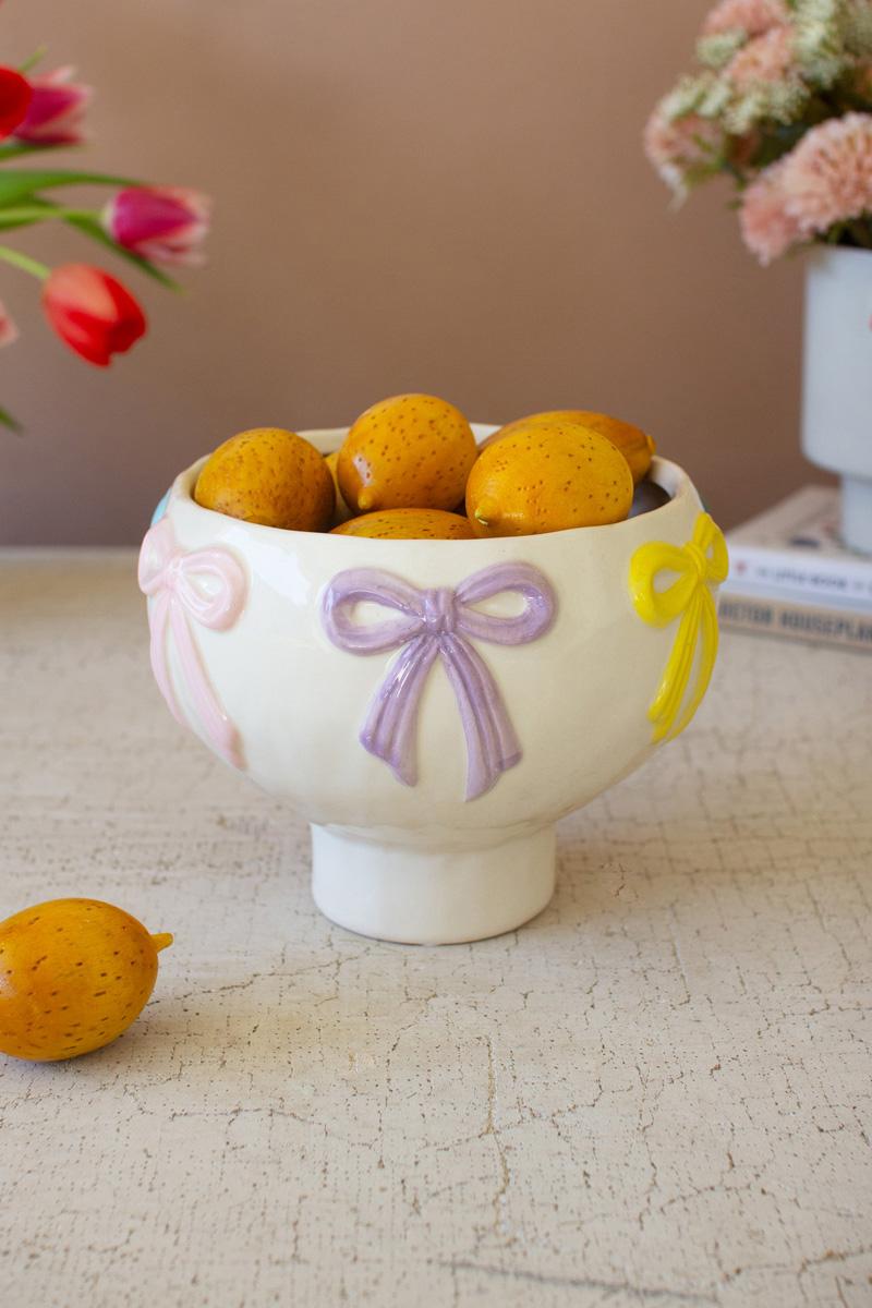 white ceramic compote bowl with bows on rim and filled with fruits