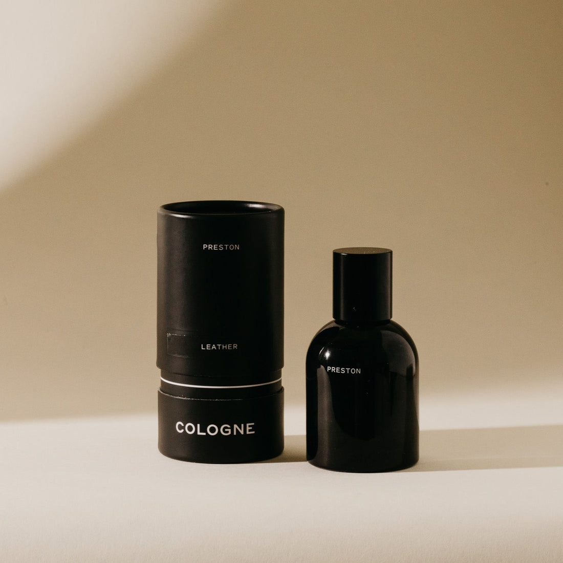 front view of leather cologne in black bottle with packaging set next to it on a beige background