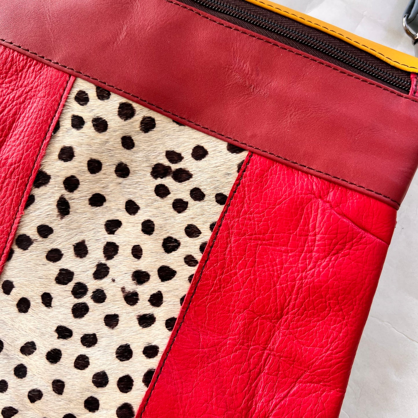close-up of red greta bag with animal print block in the center with maroon stripe and zipper across the top.