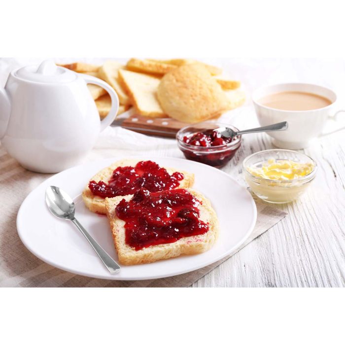 Demi spoon on a plate with toast and jam with biscuits and a teapot in the background