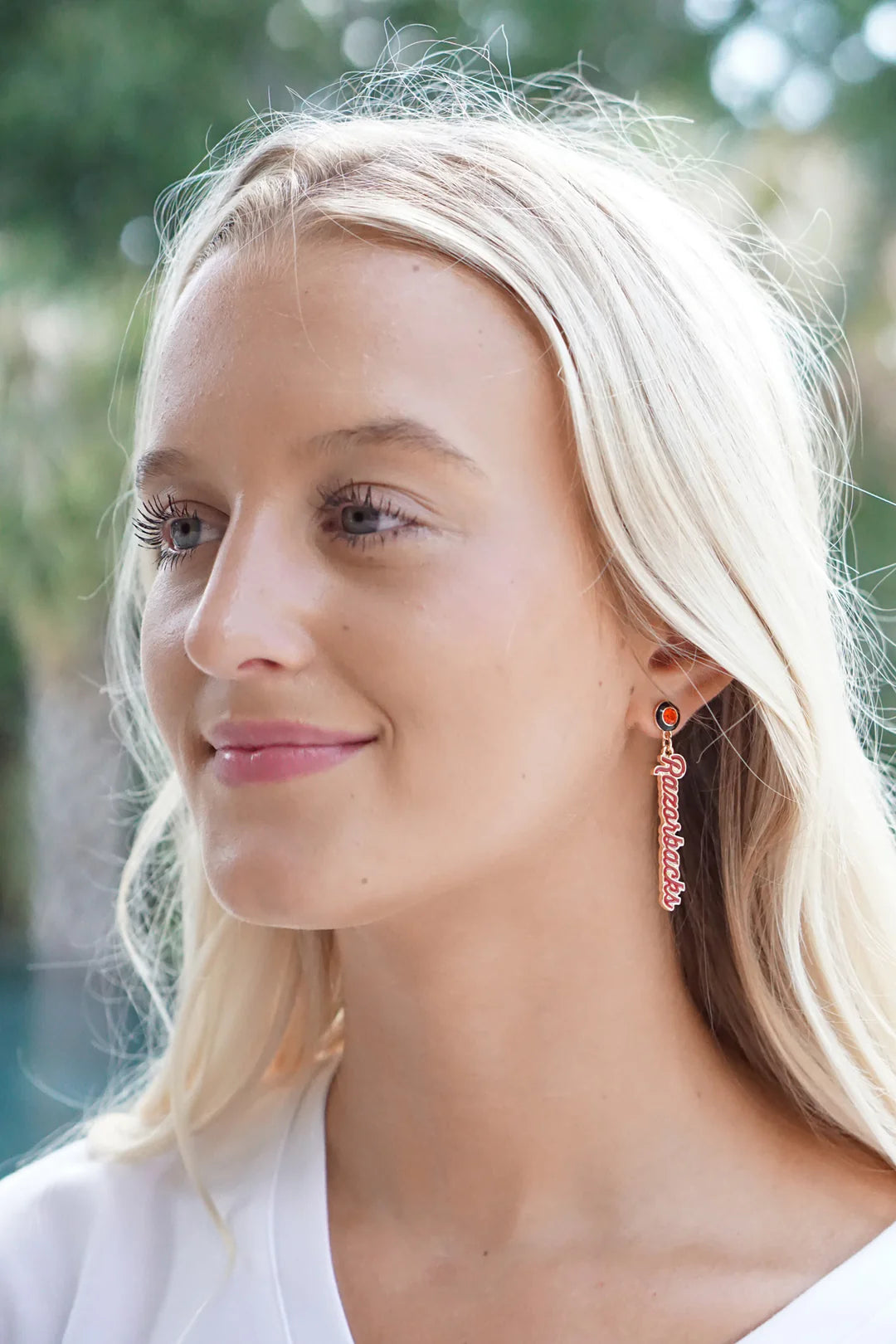 person with blonde hair wearing a white t shirt wearing Arkansas Razorbacks Autograph Enamel Earrings