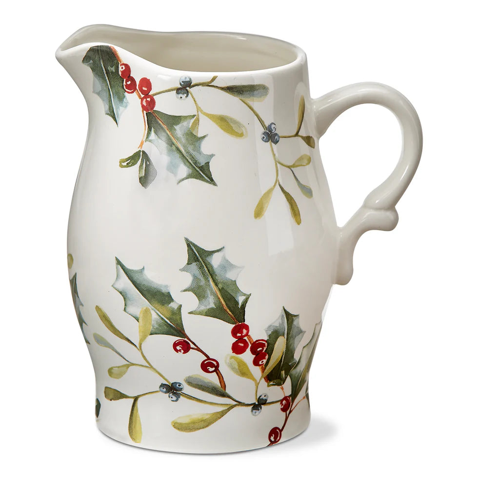 A white ceramic pitcher with a festive design, featuring green leaves, red berries, and holly.