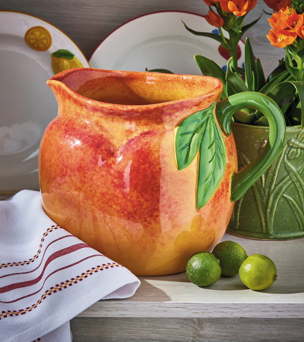 peach shaped pitcher set on a table with dishes, a pot of flowers, and limes