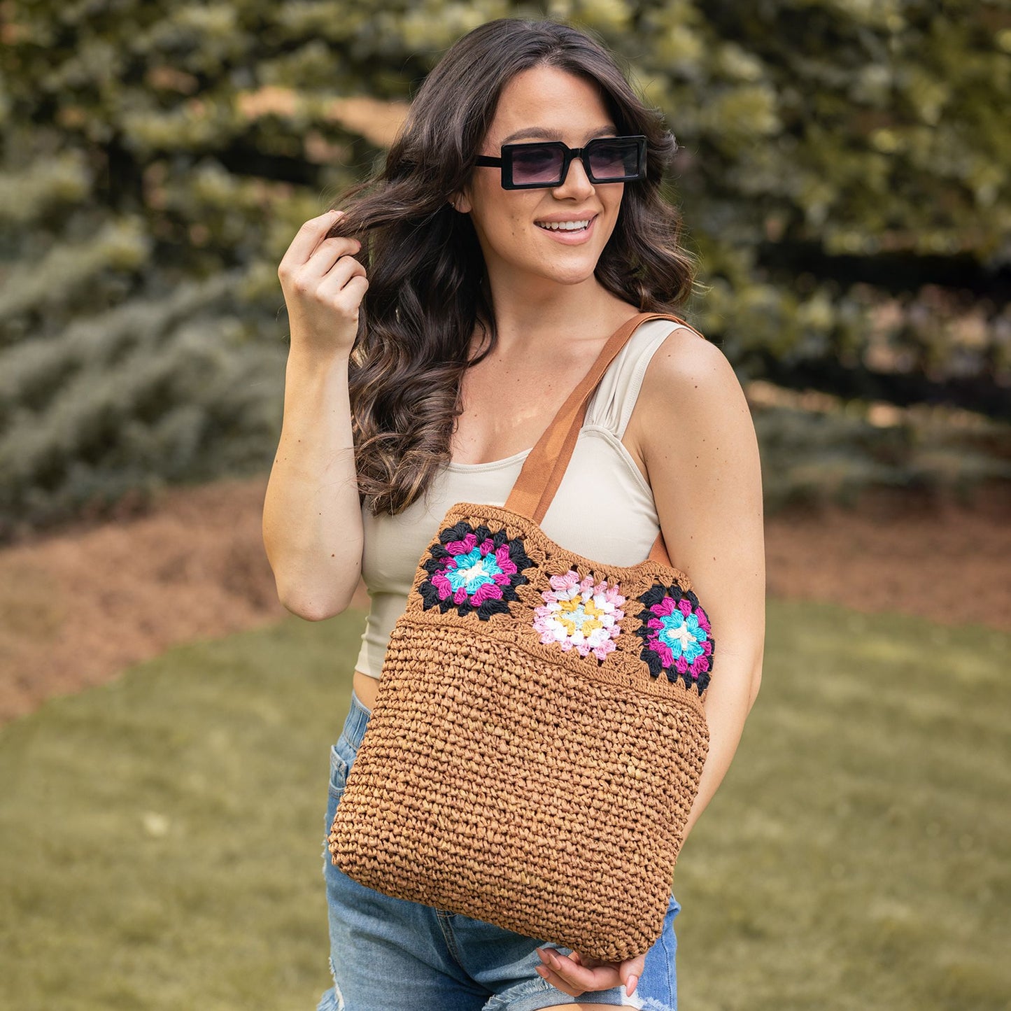 person in the park with crochet brown jute bag with granny square top boarder on their shoulder.