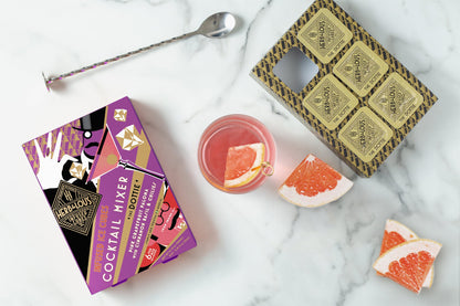 The Dottie 6 Cube Pack on a marble background arranged with grapefruit slices, a spoon, and a glass filled with Pink Grapefruit Paloma with Cinnamon Basil & Chilies.
