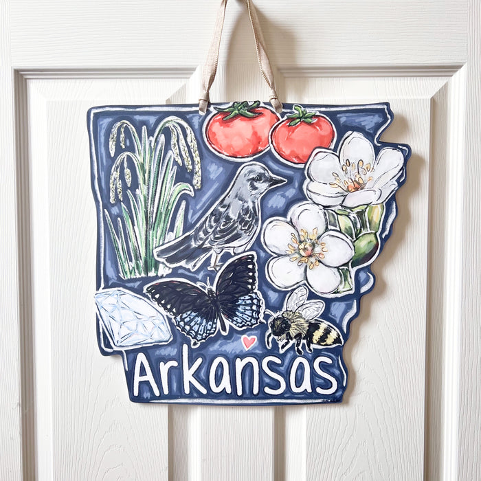 Decorative sign shaped like Arkansas with nature-themed illustrations hanging on a white door