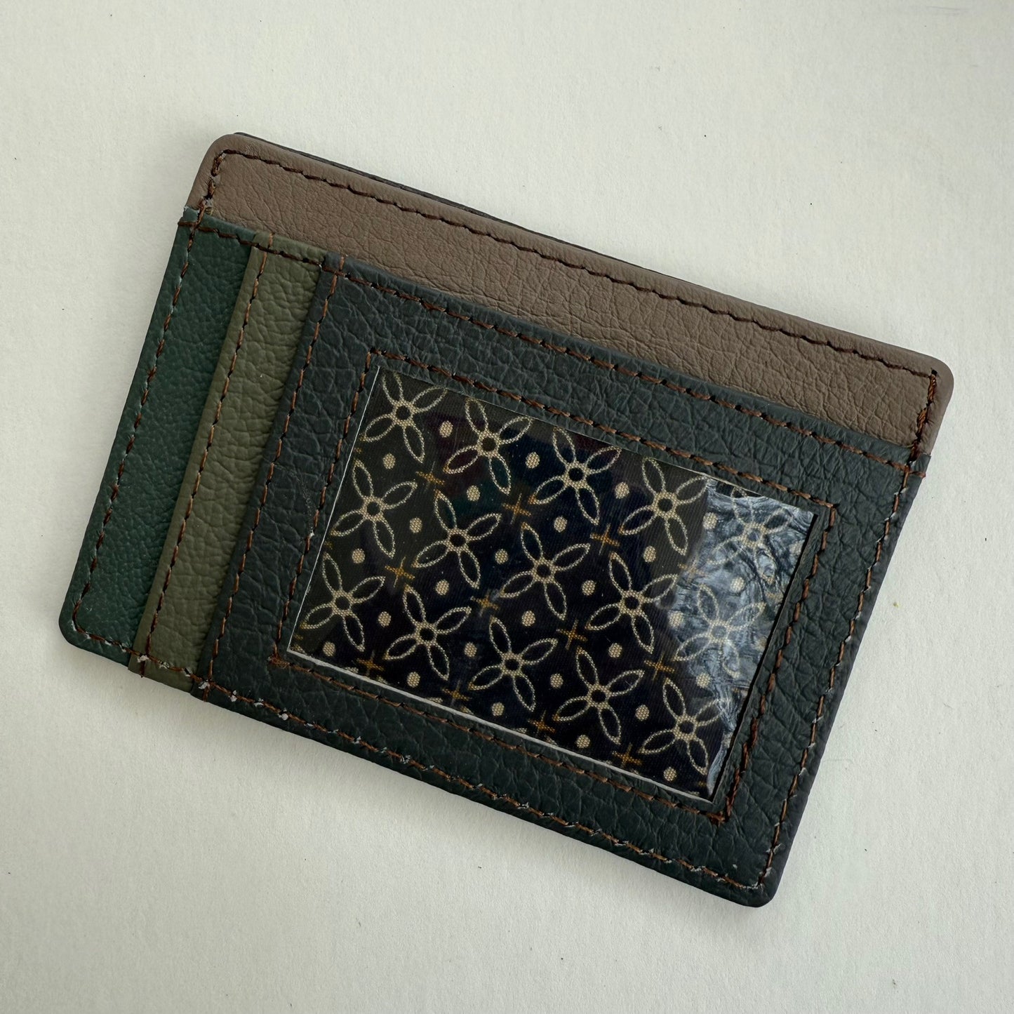 Green and brown leather cardholder with a clear ID pocket on a light gray background