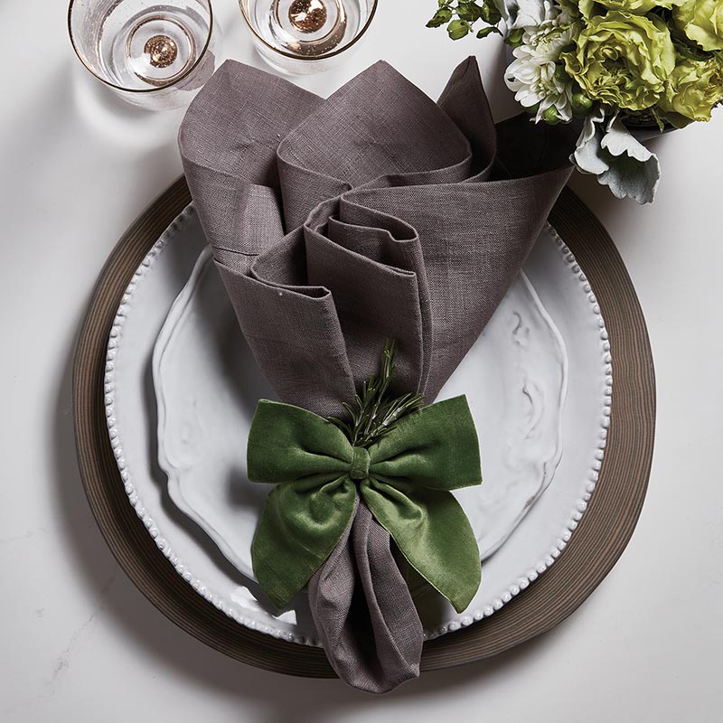 green velvet bow tie displayed on a gray napkin resting on a place setting of white plates and gray charcher