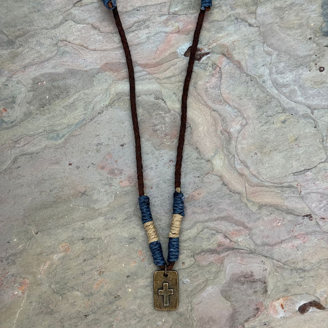Aadi Guardian Cross Necklace laying on a rock slab