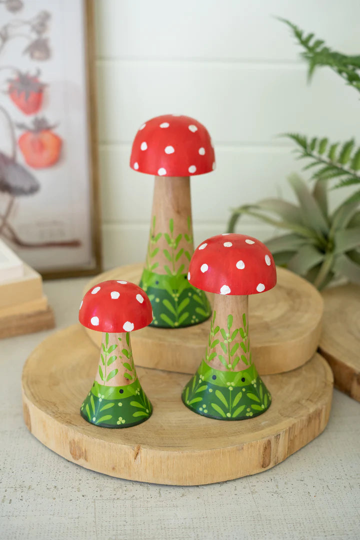 3 sizes of mushrooms arranged on a wooden riser with greenery on the background.