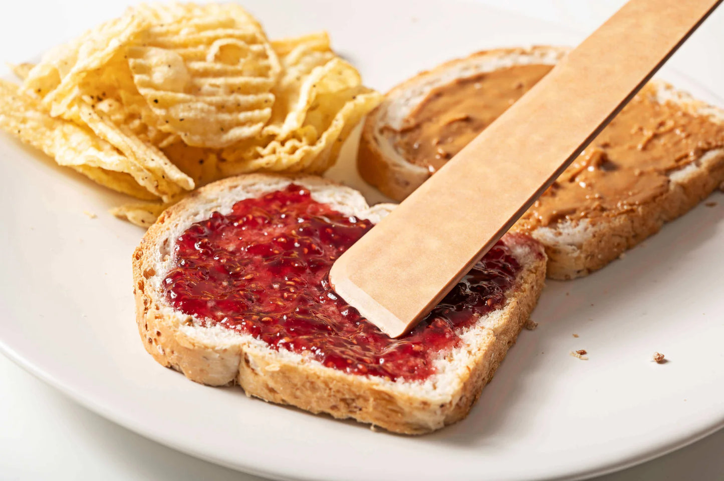 wooden utensil and Toast with peanut butter and jelly, potato chips on a white plate