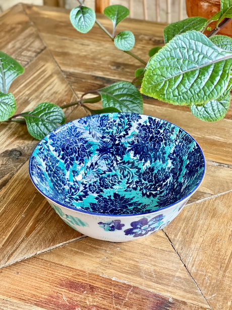 blue and torquoise bowl with an artistic pattern on a wooden table with greenery.