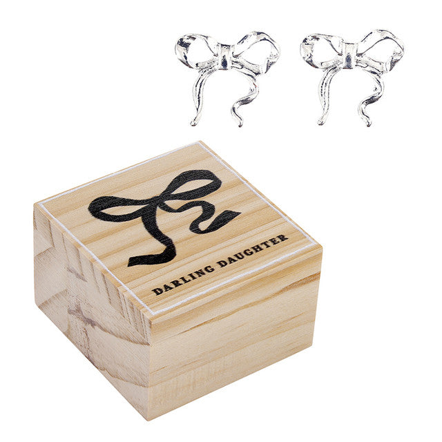 Wooden box with 'Darling Daughter' text and two silver bow-shaped earrings on a white background