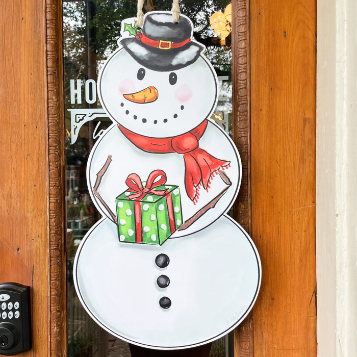 Decorative snowman holding a gift door hanger on a wooden door.