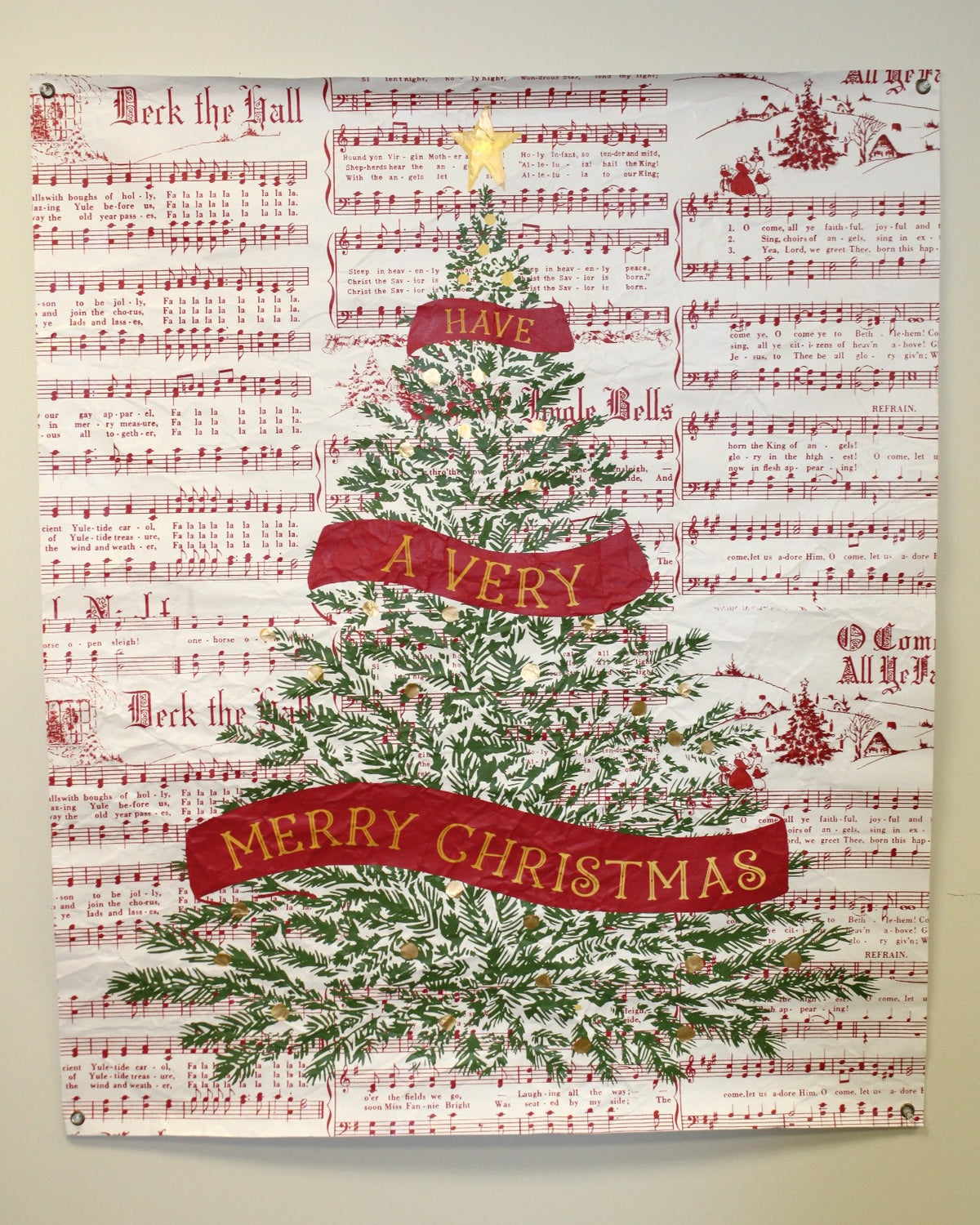 paper wall art featuring red sheet music with an image of a christmas tree with a ribbon saying have a very merry christmas
