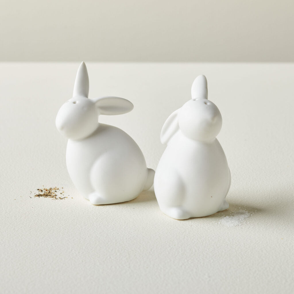 2 white ceramic bunny shaped salt and pepper shakers on a table with salt and pepper sprinkled around them.