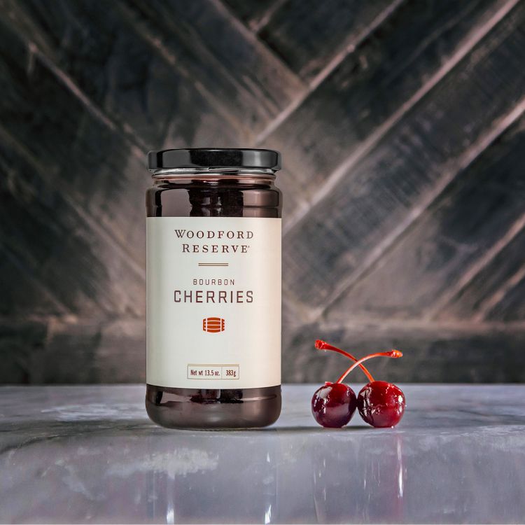 bottle of  Woodford Bourbon Cherries on a table with 2 cherries.